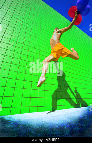 Männlich Alter 20-25 laufen und springen mit roten Luftballons in der Hand. Das Bild ist gegen eine lebendige grüne gefliesten Wand geschossen. Stockfoto