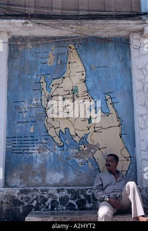 In Stone Town, die kleine Hauptstadt von Sansibar, entspannt sich ein Mann unter einer Zanzibar-Karte an eine Wand gemalt Stockfoto