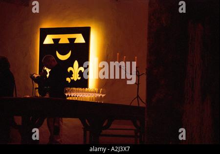 In der Alterung Fasskeller von Château Smith Haut Lafitte in Graves Pessac Leognan im Hintergrund das Wappen blazon des Schlosses mit drei französische Lilien Lilie, einen Mann steht in der Silhouette, die Verkostung ein Glas Wein, mehrere Gläser stehen auf einem Tisch und einem Kandelaber. Bordeaux Gironde Aquitaine Frankreich Europa Stockfoto