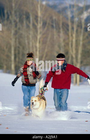 Ein Mann und eine Frau, die durch ein schneebedecktes Feld mit ihrem Hund laufen Stockfoto