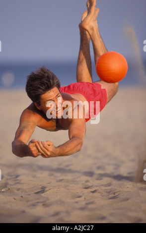 Mann tauchen, um eine orange Volleyball während eines Spiels am Strand getroffen Stockfoto