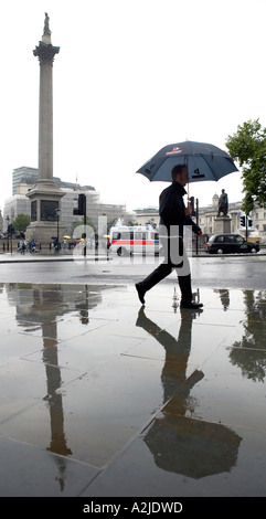 London, UK. Ein Mann geht vorbei an Nelsons Säule, Trafalgar Square, hält einen Regenschirm im Regen. Stockfoto