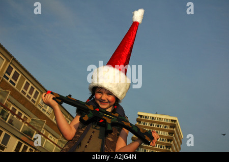 Ein Kind gekleidet in combat Kleidung und eine rote Weihnachtsmann Mütze spielen mit einem Spielzeug-Maschinengewehr. Stockfoto