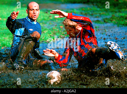 2 Fußballer Alter 20-25 Fußball spielen auf einem schlammigen Feld. Stockfoto