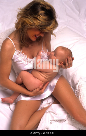Junge Mutter mit ihrem neugeborenen Kind halten und lieben das Baby im Bett kuscheln Stockfoto