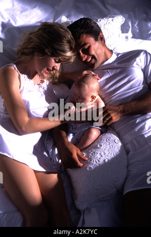 Neue Mutter und Vater im Bett mit ihrem neugeborenen Kind halten und lieben das Baby kuscheln Stockfoto