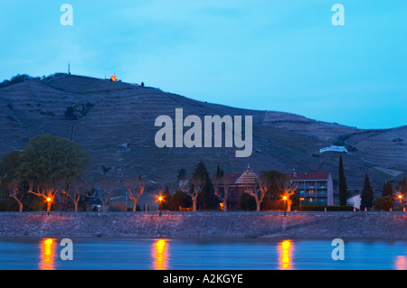 Ein Blick auf die Rhone in der blauen Sonnenuntergang Dämmerung Tain l ' Hermitage, die Kapelle auf dem Hügel Flutlicht und dem Fluss Wasser vor. Die Eremitage Weinberge auf dem Hügel hinter der Stadt Tain-l ' Hermitage, am steil abfallenden Hügel, Stein terrassenförmig angelegt. Manchmal buchstabiert Ermitage. Tain l ' Hermitage, Drome, Drôme, Frankreich, Europa Stockfoto