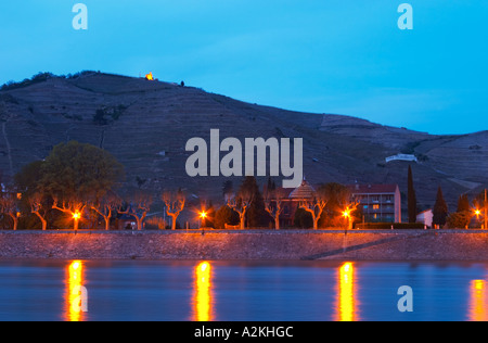 Ein Blick auf die Rhone in der blauen Sonnenuntergang Dämmerung Tain l ' Hermitage, die Kapelle auf dem Hügel Flutlicht und dem Fluss Wasser vor. Die Eremitage Weinberge auf dem Hügel hinter der Stadt Tain-l ' Hermitage, am steil abfallenden Hügel, Stein terrassenförmig angelegt. Manchmal buchstabiert Ermitage. Tain l ' Hermitage, Drome, Drôme, Frankreich, Europa Stockfoto