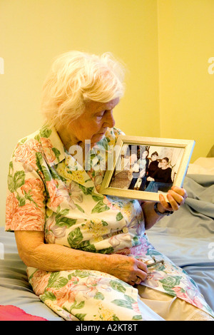 alte Dame sitzt auf der Bettkante Blick sehnsüchtig auf gerahmte Familienfoto Stockfoto