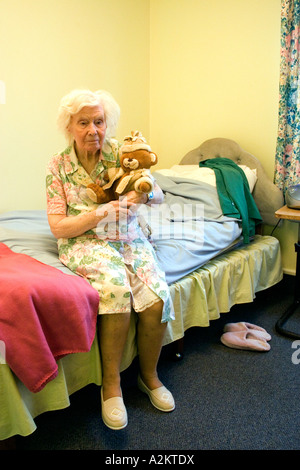 Porträt alte Dame im Pflegeheim mit Altersdemenz sitzen auf der Bettkante mit Teddybär Stockfoto