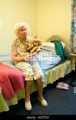 feierliche alte Dame im Pflegeheim mit Altersdemenz sitzen auf der Bettkante mit Teddybär Stockfoto