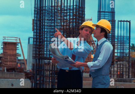 Ein japanisches und ein amerikanischer Geschäftsmann tragen Schutzhelme diskutieren und Überprüfung Pläne außerhalb einer Baustelle Stockfoto