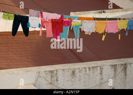 Bunte Klamotten auf einer Wäscheleine trocknen in der Sonne auf dem Dach eines Gebäudes Stockfoto