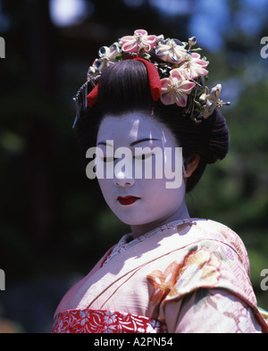 Mädchen in Maiko Lehrling Geisha Kostüm im japanischen Garten von Gion Kyoto tragen Kimono Obi Perücke Sonnenschirm Make-up Lippenstift Stockfoto