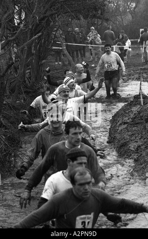 Wettbewerber waten in kaltem schlammigen Strom Tough Guy Rennen bei Tettenhall, West Midlands, England, UK Stockfoto