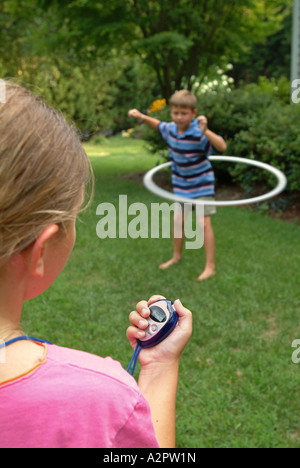 10 Jahre altes Mädchen verwendet eine digitale Stoppuhr zur Zeit 7 Jahre alten Bruder tun mit einem Hula Hoop Reifen Stockfoto