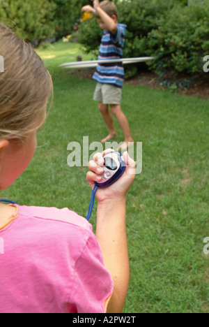 10 Jahre altes Mädchen verwendet eine digitale Stoppuhr zur Zeit 7 Jahre alten Bruder tun mit einem Hula Hoop Reifen Stockfoto