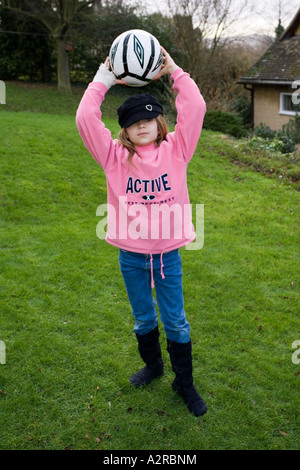 Zehn Jahre altes Mädchen mit rosa nächsten Pullover mit Fußball im Garten UK Stockfoto