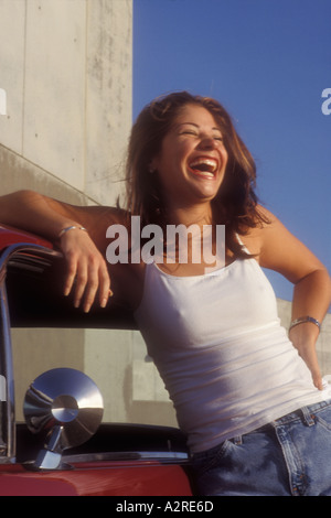18 jährige Hispanic weibliche stehende & lachend mit roten Auto Stockfoto
