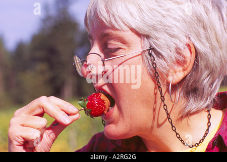 Reife behaarte grau / grau dunkelhaarige Frau mit Brille essen Schokolade getaucht Erdbeere Stockfoto