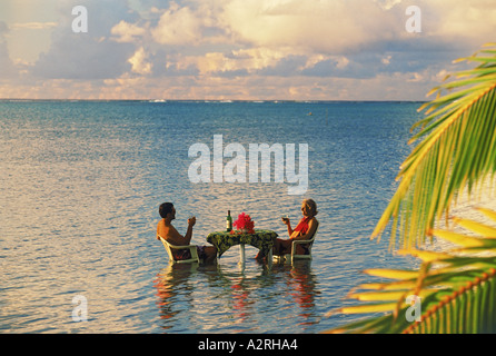 Paar sitzt am Tisch teilen Sonnenuntergang trinken in Lagune inmitten des Pazifischen Ozeans. Ruhe und Einsamkeit im Urlaubsparadies Stockfoto