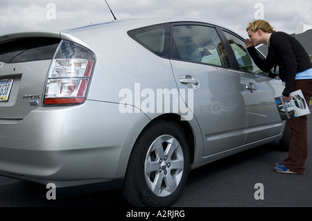 JUNGE FRAU BETRACHTEN 2004 TOYOTA PRIUS-BENZIN-ELEKTRO-HYBRID-AUTO Stockfoto