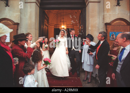 Frisch verheiratete Braut und Bräutigam, die St.-Georgs-Kirche London winkte auf Familie und Freunde zu verlassen Stockfoto