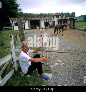 MANN STREICHELN EINEN ESEL VOR EINEM PFERDESTALL BASKENLAND FRANKREICH EUROPA Stockfoto