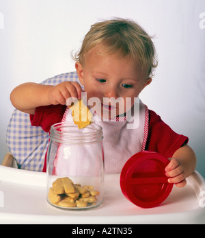 18 Monate altes Kleinkind im Hochstuhl hält Keks Stockfoto