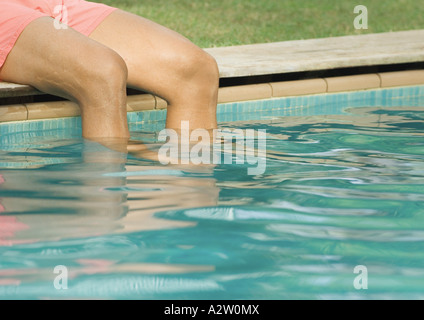 Mann, sitzend vom Rand der Swimmingpool mit Beinen im Wasser, beschnitten, Ansicht Stockfoto