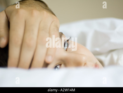 Kind im Bett mit Vaters Hand auf Stirn Stockfoto