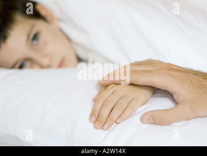 Kind im Bett liegend, auf des Kindes Vaterhand Stockfoto