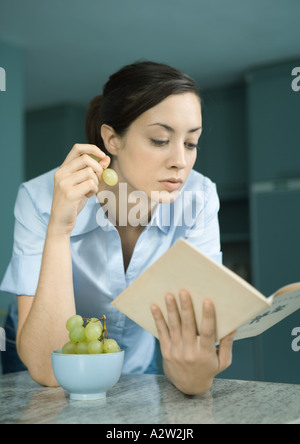 Frau Buch lesen und essen Trauben Stockfoto