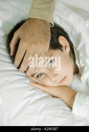 Kind im Bett liegend, des Vaters Hand auf Stirn Stockfoto