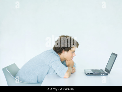 Junger Mann sitzend, stützte sich auf Schreibtisch, Laptopcomputer, denen Stockfoto