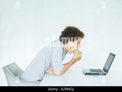 Junger Mann sitzt am Tisch, Essen Apfel und mit laptop Stockfoto