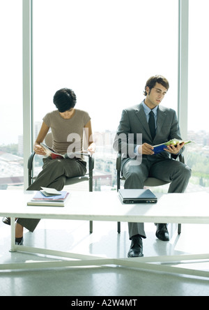 Professionelle Mann und Frau sitzen in Lobby, Blick auf Zeitschriften Stockfoto