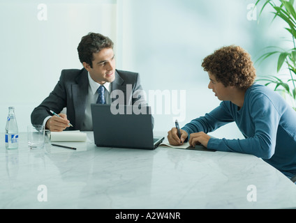 Unternehmer im Gespräch mit lässig gekleidet junge Männchen, die am Tisch sitzen Stockfoto