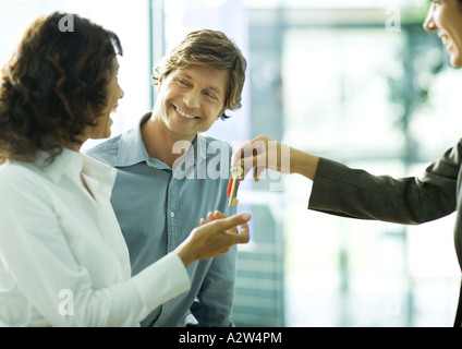 Paar Lächeln einander an, als Frau Schlüssel von Zweitfrau akzeptiert Stockfoto