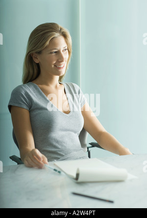 Frau sitzt am Tisch, Notizblock und Stift auf Tisch Stockfoto