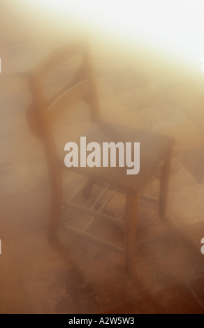 Atmosphärische Holzstuhl stehend auf einem alten Boden gefliest und überflutet mit warmem Licht von oben Stockfoto