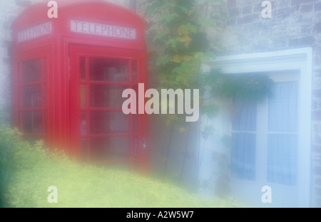 Atmosphärischen alten Stil UK rote Telefonzelle gequetscht in einer Ecke zwischen einer Hecke und Stein Ziegelhaus Stockfoto