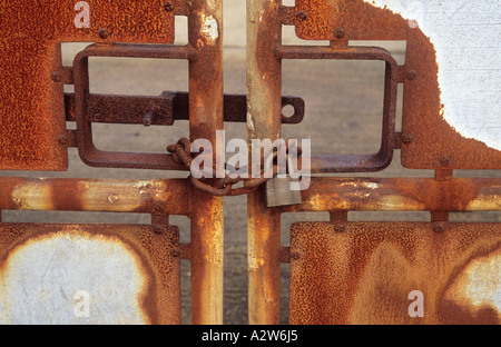 Detail der Rost Aluminium Tore geschlossen mit einer rostigen Kette und Vorhängeschloss mit Beton gehalten zusammengesetzte hinter Stockfoto