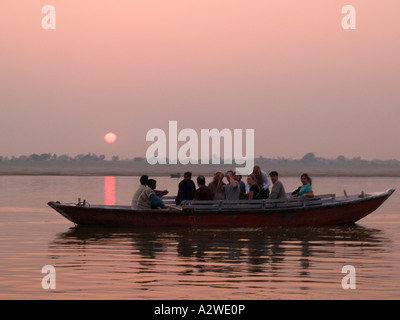 Sonnenaufgang über dem Fluss Ganges mit Ruderboot mit westlichen Touristen auf Sightseeing-Trip im Morgengrauen Varanasi Stockfoto