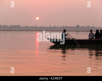 Sonnenaufgang über dem Fluss Ganges mit Ruderboot mit westlichen Touristen auf Sightseeing-Trip im Morgengrauen Varanasi Stockfoto