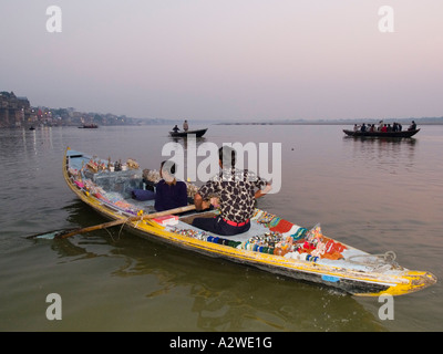 Indische Männer im Ruderboot mit Souvenirs, im Anschluss an Touristen im Morgengrauen-Sightseeing-Trip am Fluss Ganges Varanasi zu verkaufen Stockfoto