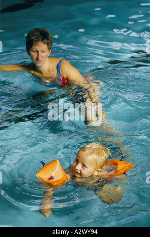Eine junge Mutter hilft ihr Kleinkind in einem Pool tragen Armbinden schwimmen lernen Stockfoto