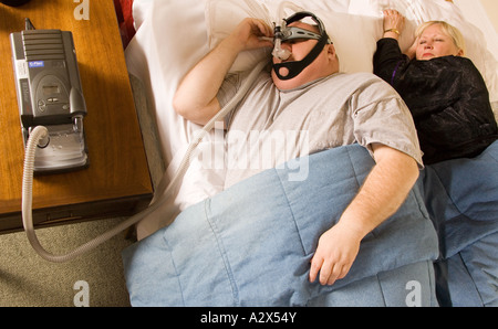 Mann und Frau im Bett zu schlafen versuchen. Der Mann trägt ein CPAP-Gerät - Continuous Positive Airway Pressure Stockfoto