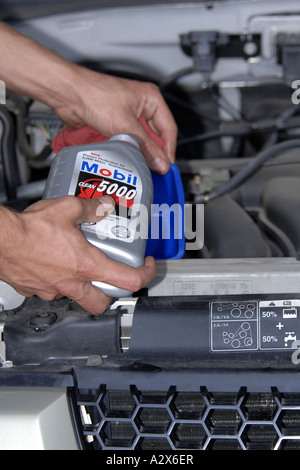 Einen männlichen Fahrzeug-Techniker füllt sich ein Motor mit Öl in einer schnellen Service Garage Stockfoto
