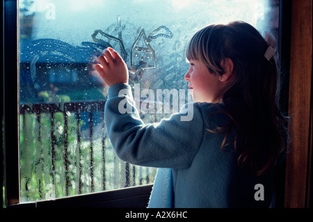 Kinder. Kleines Mädchen im Innenbereich mit Fingern auf feuchten Fensterscheibe zeichnen. Stockfoto